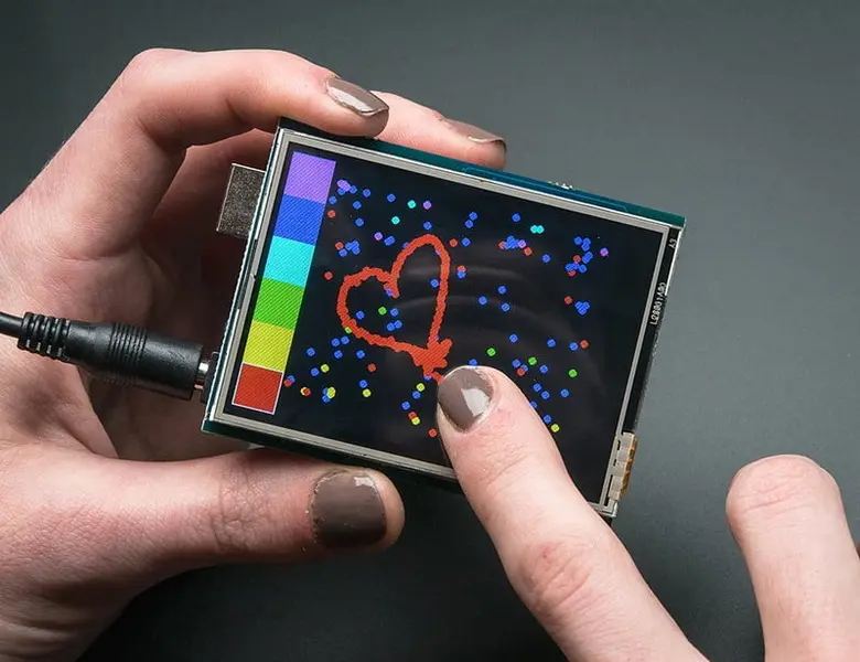 يتم استخدام شاشة تعمل باللمس مقاومة لرسم قلب على خلفية تفاعلية ملونة أثناء حملها بين يدي الشخص